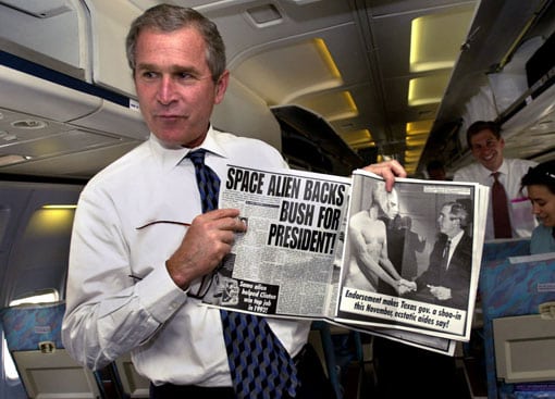 George W. Bush enseña el artículo del 'Weekly World News' en el que se dice que los extraterrestres apoyan su candidatura presidencial, en su avión de campaña en mayo de 2000. Foto: AP.